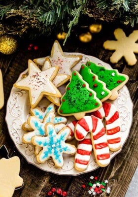 A batch of decorated cut out sugar cookies on a white plate on a wooden background.
