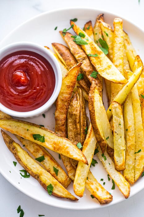 Close-up view of a white plate of crispy french fries with ketchup
