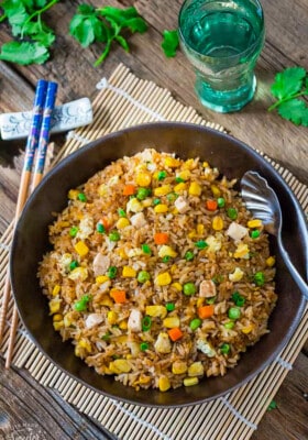 Egg fried rice in a black bowl with a spoon beside a pair of chopsticks and a glass of water