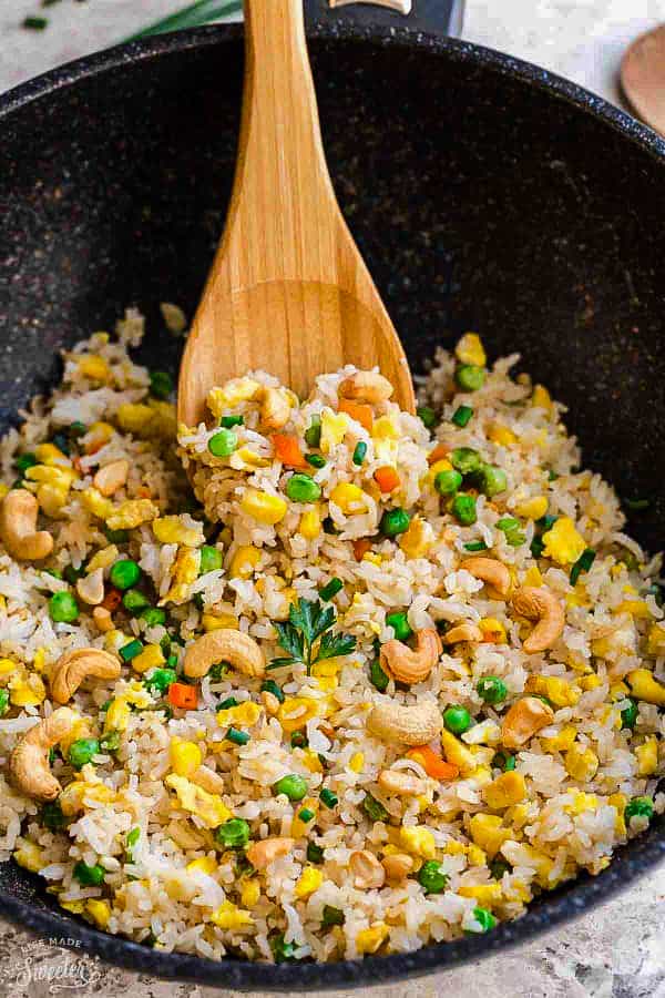 A wok full of fried rice with a wooden serving spoon scooping some out