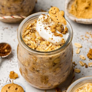 A jar of Gingerbread Overnight oats topped with a dollop of cream and cookie crumbs