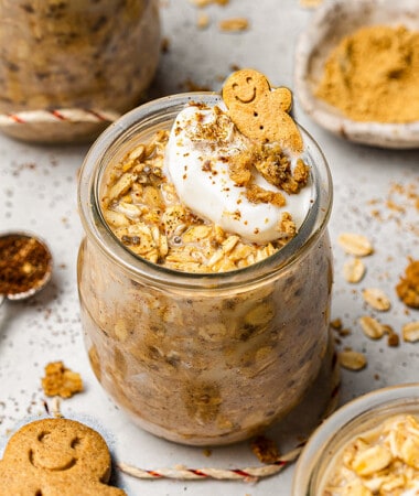 A jar of Gingerbread Overnight oats topped with a dollop of cream and cookie crumbs