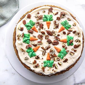 Overhead view of a decorated and frosted carrot cake on a white cake stand