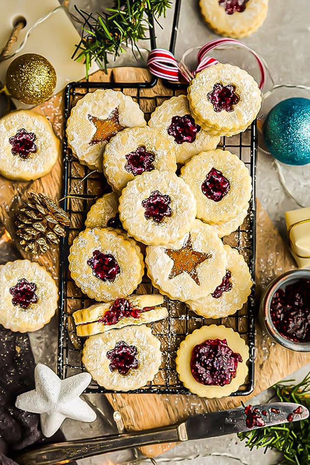 A batch of gluten free Linzer cookies layered over each other on a black wire rack surrounded with ornaments.