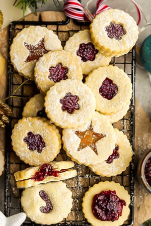 Close-up of a batch of gluten free Linzer cookies layered over each other on a black wire rack surrounded with ornaments.