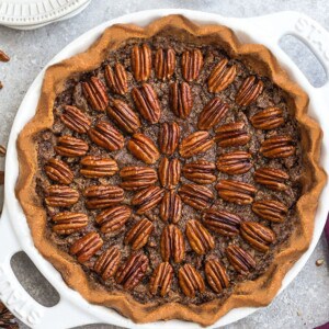 An entire gluten-free pecan pie in a white pie plate on a grey background.