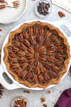 An entire gluten-free pecan pie in a white pie plate on a grey background.
