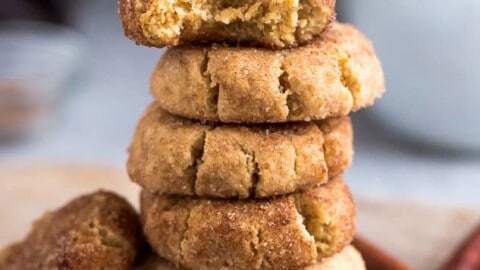 Side view of 6 stacked gluten free snickerdoodles cookies on a wire rack on a grey background with a bite