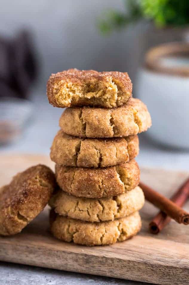 Side view of 6 stacked gluten free snickerdoodles cookies on a wire rack on a grey background with a bite