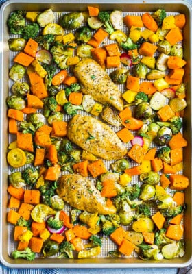 Top view of three baked chicken breasts surrounded with chopped fall vegetables on a baking sheet