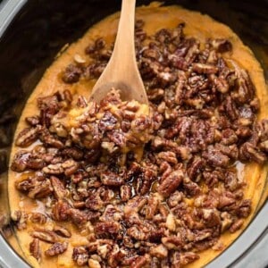 An entire batch of healthy sweet potato casserole in a black oval slow cooker with a wooden spoon.