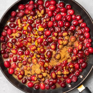 Overhead view of fresh cranberries with water and cinnamon in a skillet