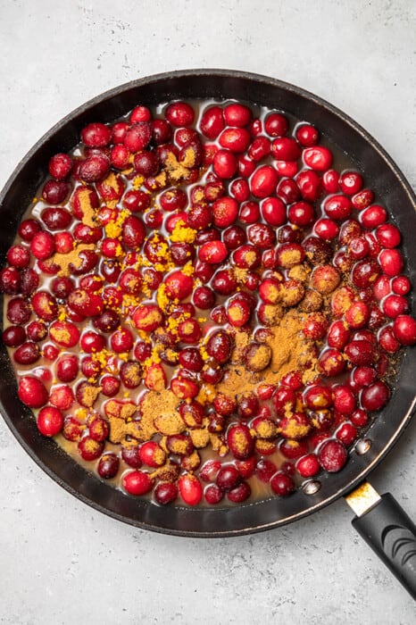 Overhead view of fresh cranberries with water and cinnamon in a skillet