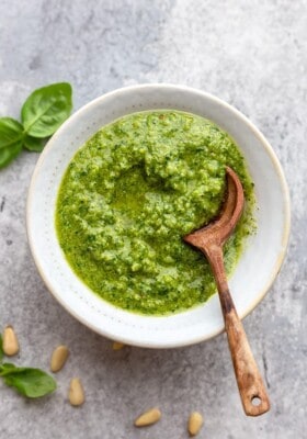A serving of homemade pesto in a white bowl with a wooden spoon