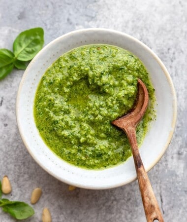 A serving of homemade pesto in a white bowl with a wooden spoon