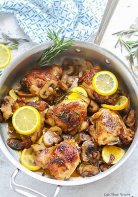 Four seared lemon rosemary chicken thighs in a skillet with sautéed mushrooms and lemon slices.