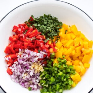 A bowl with ingredients to make mango salsa: diced mango, cilantro, jalapeno, bell peppers, garlic and red onions