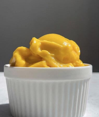 Side shot of a serving of mango sorbet in a white ramekin bowl