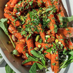 A batch of maple glazed carrots in an oval serving platter with fresh herbs and pistachos