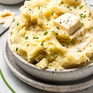 A close-up shot of a bowl containing vegan mashed potatoes topped with a pat of vegan butter and chopped chives