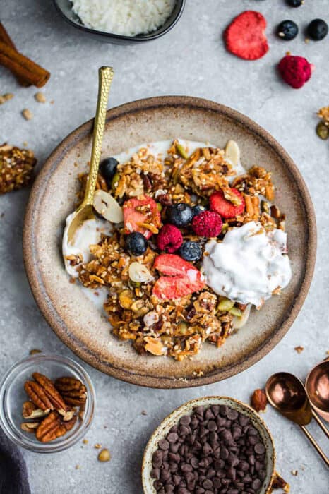 Top view of paleo granola in a white bowl with a gold spoon and coconut yogurt