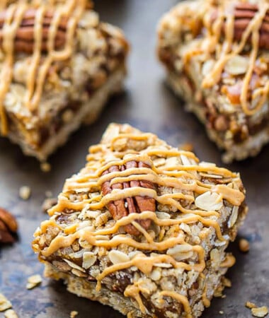 A peanut butter oatmeal bar topped with a whole pecan and a peanut butter drizzle
