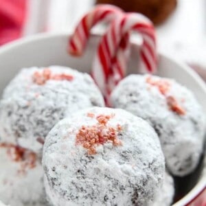 A pile of four peppermint snowball cookies in a white bowl with candy canes.