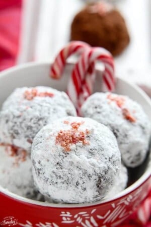 A pile of four peppermint snowball cookies in a white bowl with candy canes.