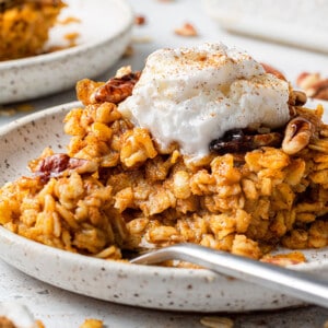 A close-up shot of a piece of pumpkin baked oatmeal on a plate with yogurt and a pinch of cinnamon on top