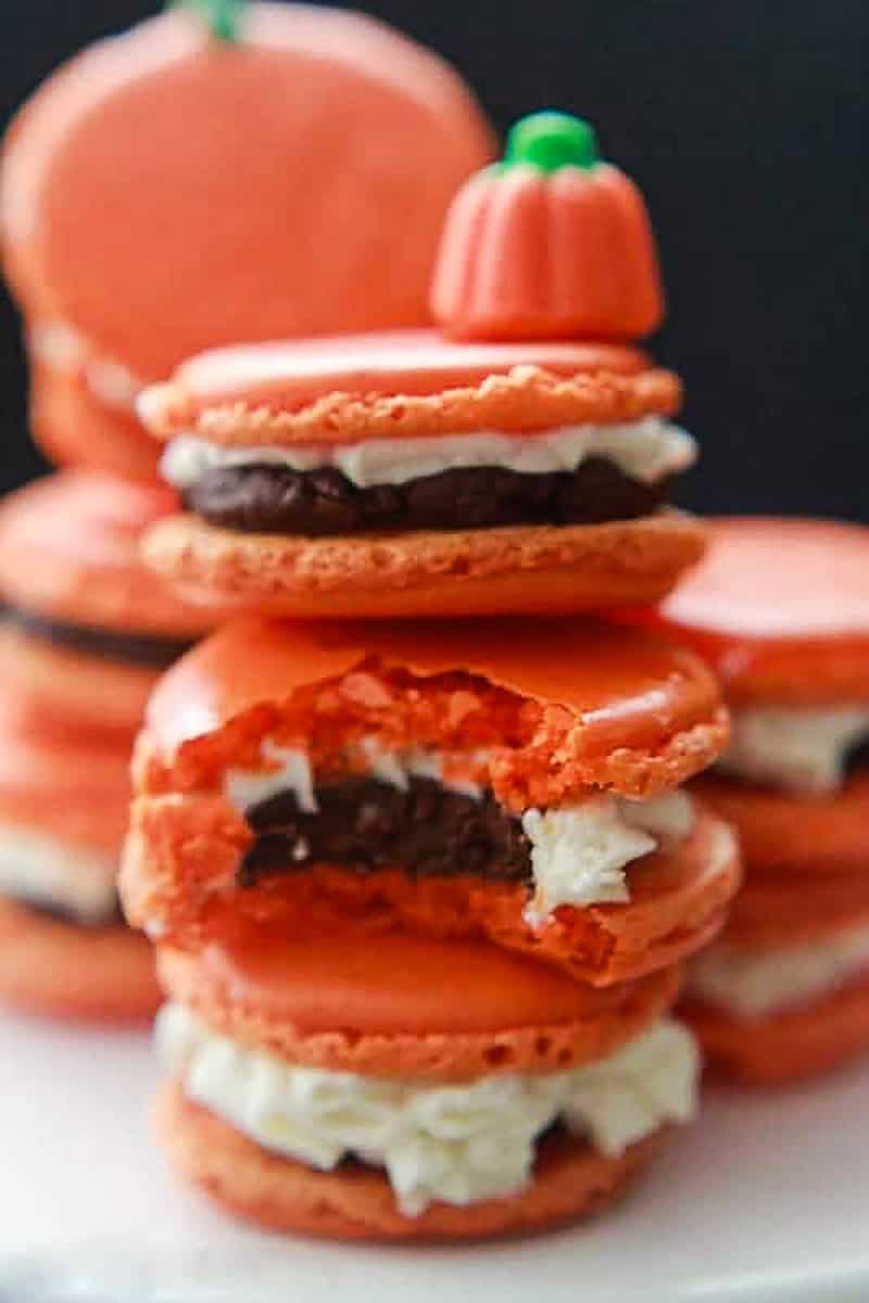 Three pumpkin macarons stacked on top of each other, one macaron has a bite.