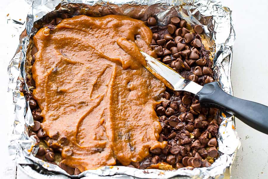 Pumpkin being spread over chocolate chips in a foil-lined pan
