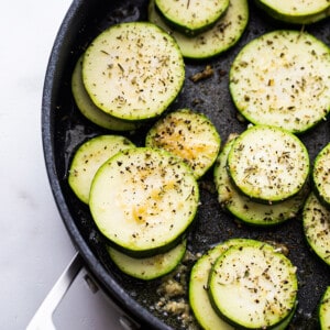 Top view of raw zucchini rounds with salt and black pepper in a large nonstick pan