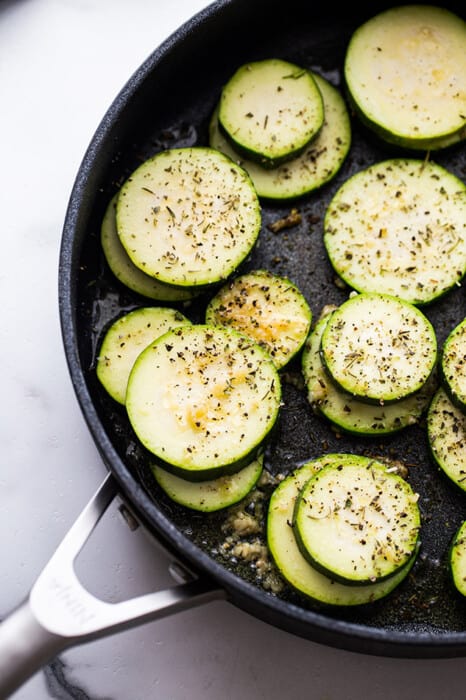 Top view of raw zucchini rounds with salt and black pepper in a large nonstick pan