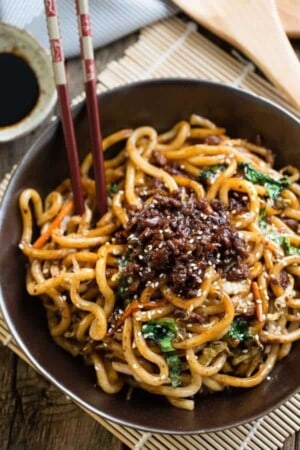 A bowl of Shanghai stir fried noodles topped with ground pork in a black bowl with chopsticks