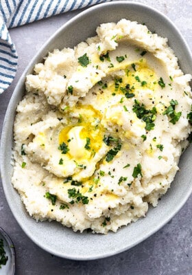 A serving of slow cooker mashed potatoes topped with melted butter in an oval bowl.