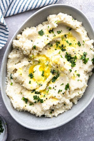 A serving of slow cooker mashed potatoes topped with melted butter in an oval bowl.