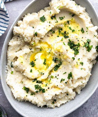 A serving of slow cooker mashed potatoes topped with melted butter in an oval bowl.