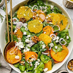 Spinach Orange Salad in a white bowl with gold serving spoons
