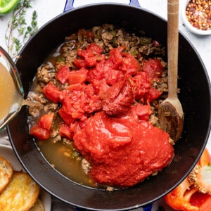 Ground turkey, tomato paste and crushed tomatoes in a blue dutch oven / pot with a wooden spoon