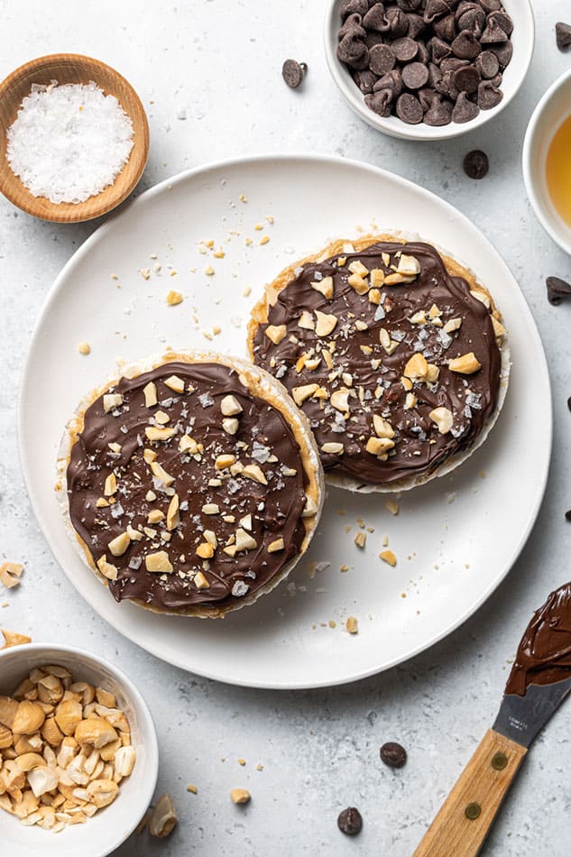 Two loaded frozen TikTok chocolate peanut butter rice cakes topped with cashew butter, cashews and melted chocolate on a white plate