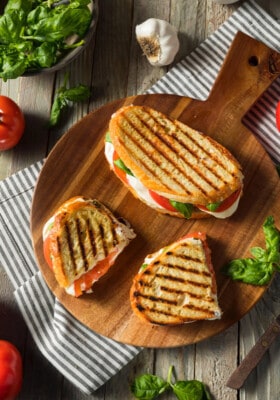 Three servings of grilled cheese sandwich (mozzarella, tomatoes and basil) on a rustic wooden board
