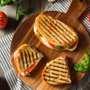 Three servings of grilled cheese sandwich (mozzarella, tomatoes and basil) on a rustic wooden board