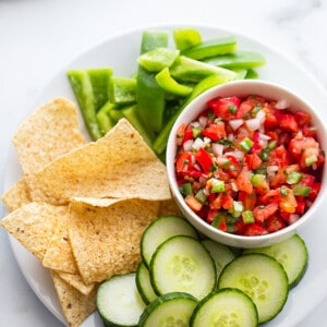 Top view of a bowl of fresh tomato salsa served with sliced cucumbers, bell peppers and chips