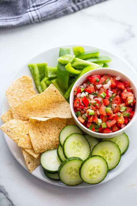 Top view of a bowl of fresh tomato salsa served with sliced cucumbers, bell peppers and chips