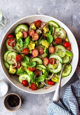Top view of tossed cucumber tomato salad in a white bowl with a fork