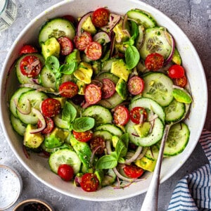 Top view of tossed cucumber tomato salad in a white bowl with a fork