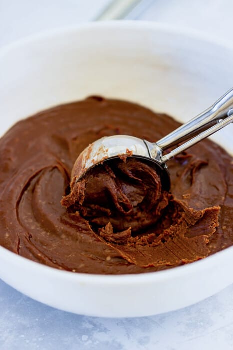 A cookie scoop digging into a bowl of chocolate truffle filling