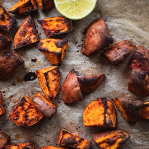 Roasted sweet potatoes on a parchment-lined baking sheet with half of a fresh lime