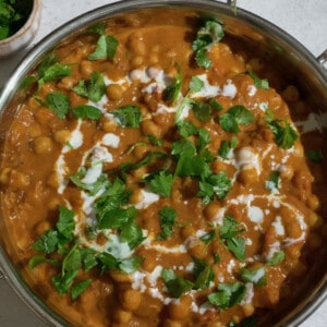 A stainless steel pot of chickpea curry with topped with coconut milk and herbs