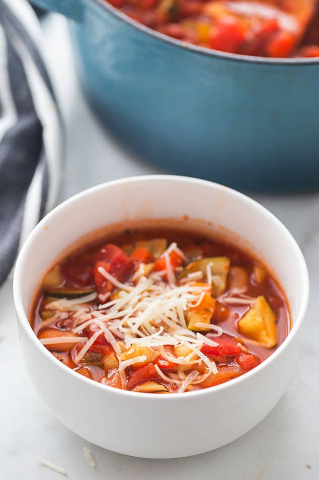 A serving of vegan minestrone soup in a white bowl with grated cheese
